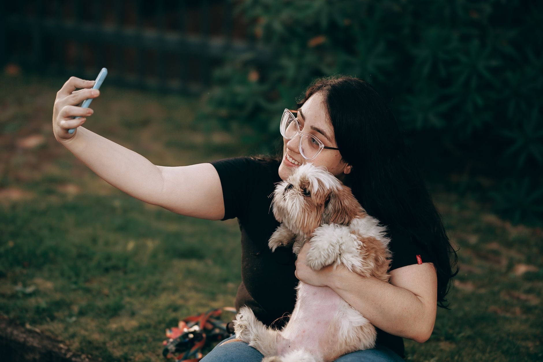 Kobieta robi selfie z psem rasy shih tzu podczas spaceru w parku